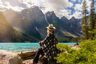 Woman sitting on a rock looking out at lake. In the distance is a large mountain range